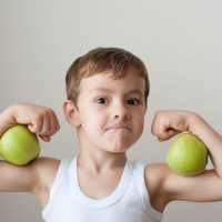 Boy with green apples showing biceps after strength training