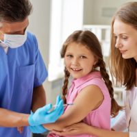 Male doctor vaccinating a little girl with her mother close by