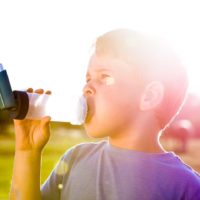 Boy using inhaler for asthma in village with sunset suffering from allergies