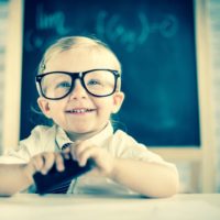 Child genius sat at desk in shcool with glasses on looking very intelligent