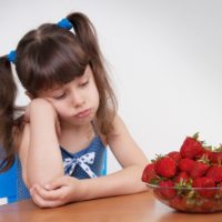 Girl sadly looks at the plate with strawberries
