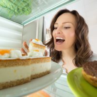 Hungry young woman choosing slice of cake as comfort food from the fridge