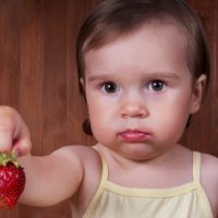 Toddler holding out a strawberry and upset because of allergy