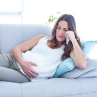 Sad pregnant woman lying on sofa suffering from depression