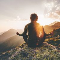 Man meditating at sunset in the mountains