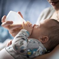 Young infant drinking baby formula from bottle whilst lying back on monthers chest