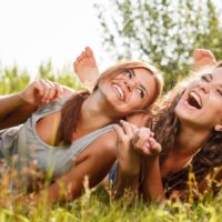 Two girlfriends in T-shirts lying down on grass laughing having good time