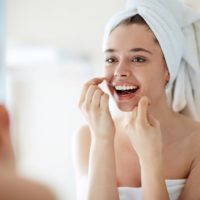 Woman flossing her teeth clean in front of the mirror