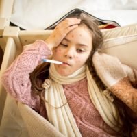 Portrait of sick girl with chickenpox lying in bed and measuring temperature