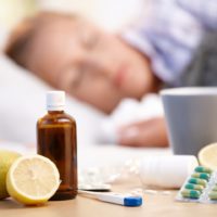 Vitamins, medicines and hot tea in front of woman with a cold sleeping in background