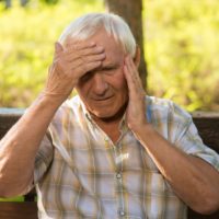 Senior man holding his head because he is having a stroke and needs to call an ambulance