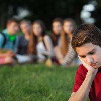 Teenage boy feeling sad being watched by a group of friends in the background