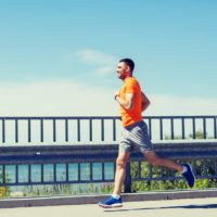 Smiling young man with heart rate watch running at summer seaside