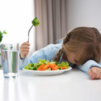 girl with head on table and fork of broccoli