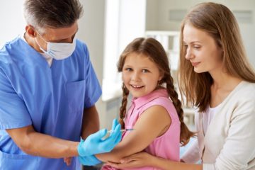 Male doctor vaccinating a little girl with her mother close by