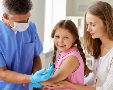 Male doctor vaccinating a little girl with her mother close by