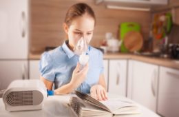 Girl with asthma using inhaler and reading book in the kitchen