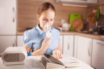Girl with asthma using inhaler and reading book in the kitchen