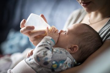 Young infant drinking baby formula from bottle whilst lying back on monthers chest