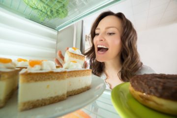 Hungry young woman choosing slice of cake as comfort food from the fridge