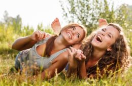 Two girlfriends in T-shirts lying down on grass laughing having good time