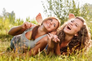 Two girlfriends in T-shirts lying down on grass laughing having good time