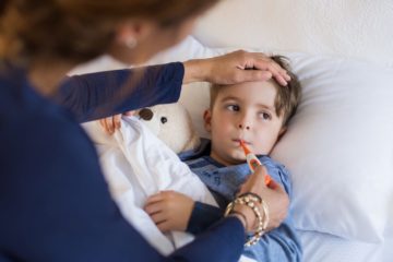 Mother checking temperature of her sick son who has thermometer in his mouth