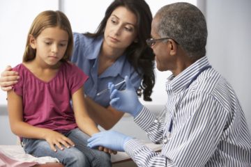 Doctor administering a vaccination to a young girl whilst being comforted by her mother