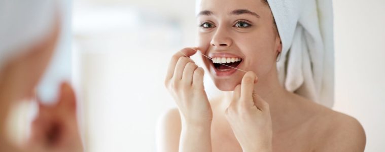 Woman flossing her teeth clean in front of the mirror