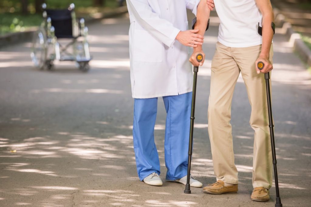 Close-up of doctor helping to his patient with osteoporosis to walk with crutches