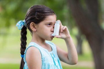 Little girl using her asthma inhaler on a sunny day