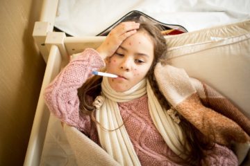 Portrait of sick girl with chickenpox lying in bed and measuring temperature