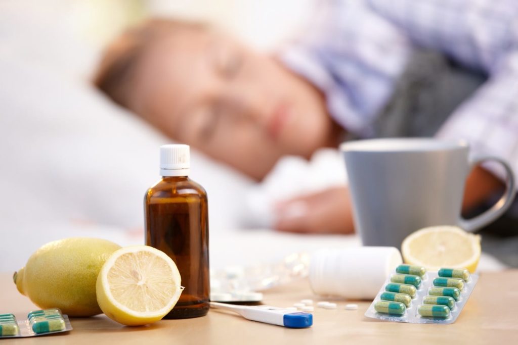 Vitamins, medicines and hot tea in front of woman with a cold sleeping in background