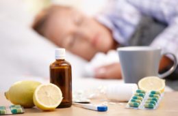 Vitamins, medicines and hot tea in front of woman with a cold sleeping in background