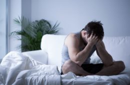 Man with depression sat on bed with head in his hands