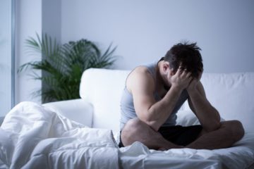 Man with depression sat on bed with head in his hands