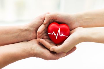 Mans hand donating a red heart organ with cardiogram to woman