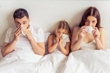 Parents and their daughter suffering from a cold wiping noses while lying on bed