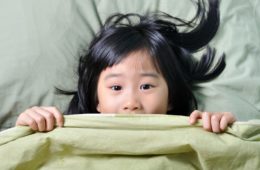 Scared little asian girl having childhood nightmares and hiding behind blanket