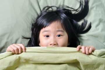 Scared little asian girl having childhood nightmares and hiding behind blanket