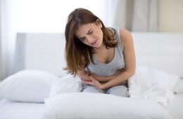 Woman sat on bed feeling constipated