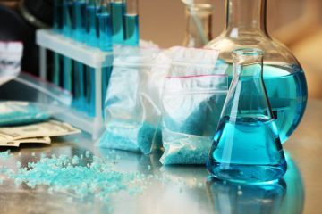 Blue methamphetamine and liquid in flasks on table in laboratory