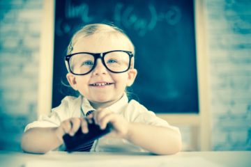 Child genius sat at desk in shcool with glasses on looking very intelligent