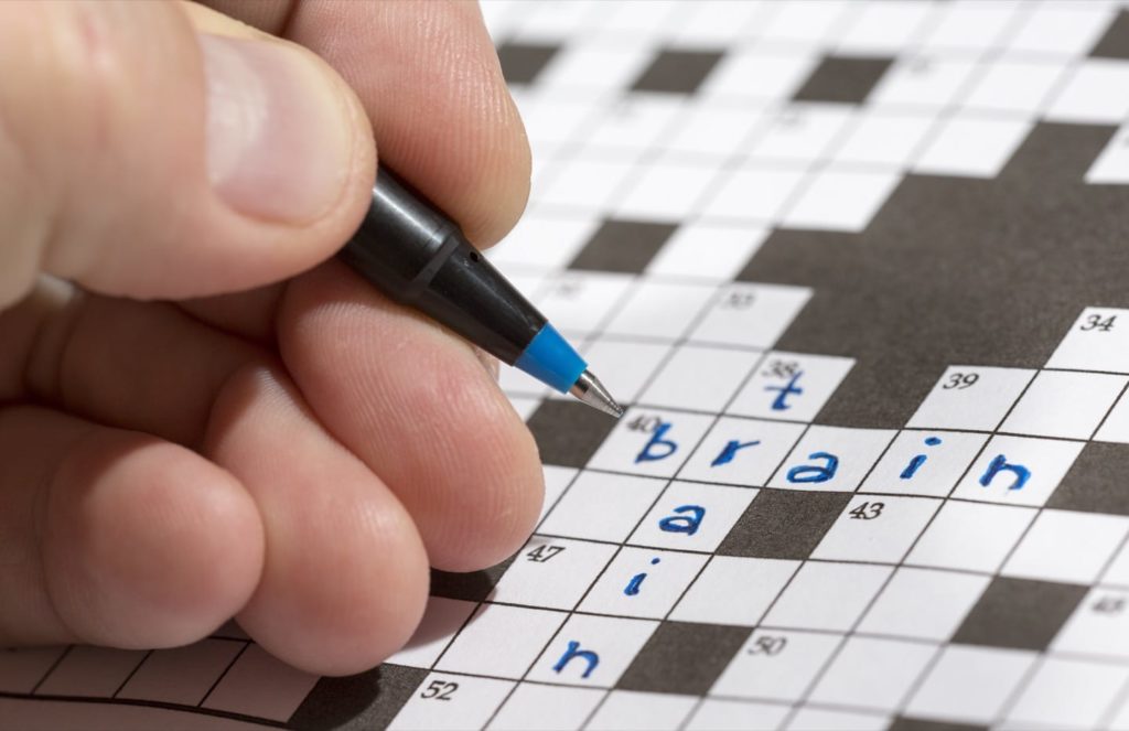 Man is holding a pencil in his hand and there are words 'train' and 'brain' already written in the crossword