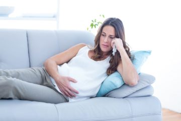 Sad pregnant woman lying on sofa suffering from depression