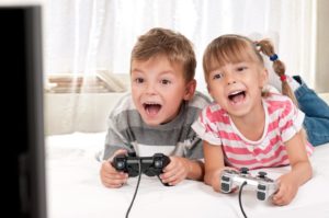 Young boy and girl lying on a bed enjoying playing video games together
