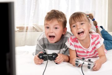 Young boy and girl lying on a bed enjoying playing video games together