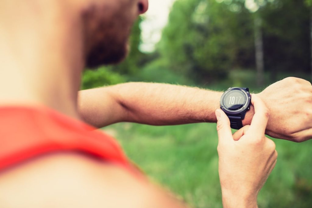 Man interval training on mountain forest trail checking looking at stopwatch smart watch