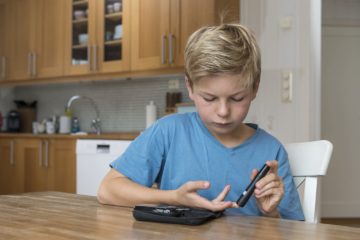 Child with diabetes measuring glucose or blood level in a kitchen