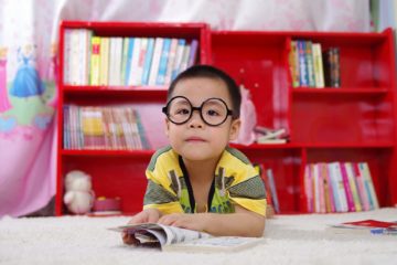 boy with eyeglasses in front of bookshelf